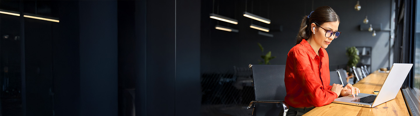 Junge Geschäftsfrau, die an einem Schreibtisch im Büro mit Blick auf die Stadt an ihrem Laptop arbeitet