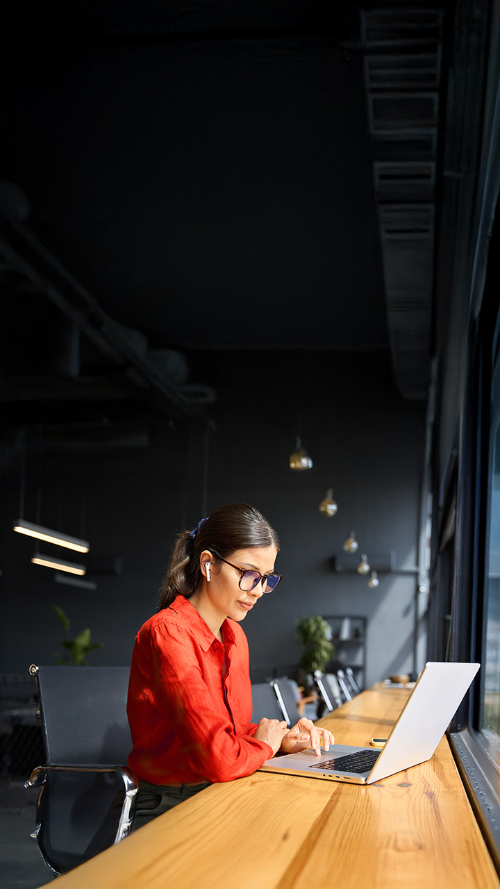 Junge Geschäftsfrau, die an einem Schreibtisch im Büro mit Blick auf die Stadt an ihrem Laptop arbeitet