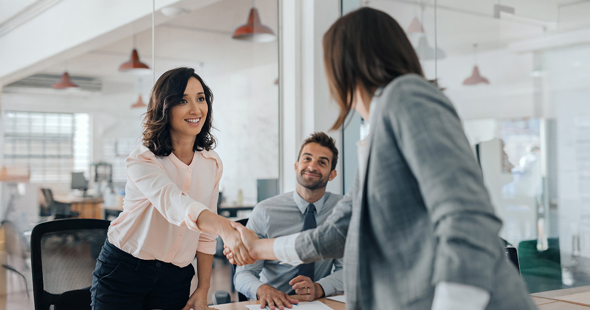 Smiling young businesswoman shaking hands with an office colleague